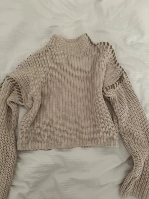 Beige stickad tröja från Vero Moda - Snygg beige stickad tröja från Vero Moda med hög krage och coola detaljer i form av gröna inslag längs axlarna. Tröjan har en boxy passform och långa ärmar, perfekt för lager-på-lager-stil. Materialet är mjukt och grovstickat.