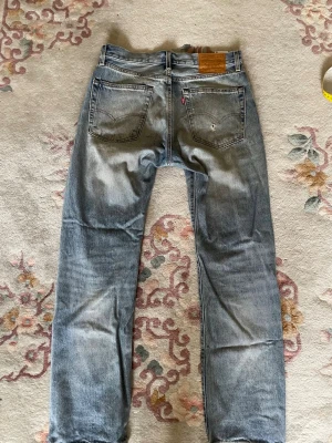 Levi's 551 ljusblå raka jeans W31 - L32  - Säljer ett par klassiska ljusblå jeans från Levi's med raka ben och femficksmodell. Jeansen har slitningar och en vintage tvätt, samt läderpatch bak i midjan. Perfekta för en avslappnad och trendig look.