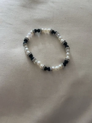 Svartvitt pärlarmband med detaljer - Fint armband med vita och svarta pärlor med små silvriga detaljer. Armbandet har en elastisk tråd som gör det enkelt att ta på och av. 