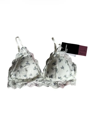 Vit spets-bh med blommigt mönster H&M - Söt vit bh från H&M med små blå blommor och ribbad struktur. Bh:n har spetskant runt kuporna och nedtill, samt justerbara axelband. Mjuk och utan bygel. Nypris 149kr