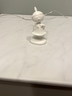 Vit Lilla My figur i keramik - Säljer en vit keramikfigur föreställande Lilla My från Mumin. Figuren har en rund bas, tydliga detaljer i håret och klänningen samt armarna i sidorna. Perfekt som dekoration eller samlarobjekt för Mumin-fans.