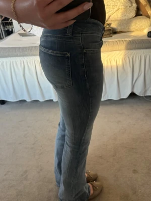 Blå bootcut jeans med låg midja - Snygga blå bootcut jeans med låg midja och klassiska fem fickor. Jeansen har en lätt tvättad look och sitter tajt över låren för att sedan bli vidare nedtill. Perfekta för dig som gillar en avslappnad men trendig stil.
