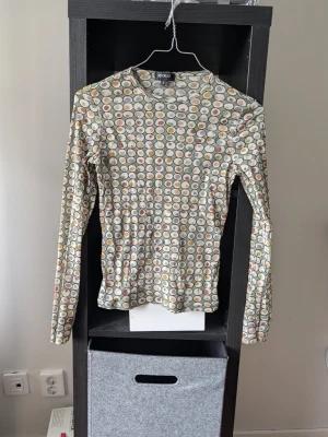 Mönstrad mesh-top från Kookai - Säljer en långärmad mesh-top från Kookai med coolt cirkelmönster i grönt, gult, lila och beige. Tunn och stretchig med rund halsringning. Hål på baksidan av kragen och lös tråd på ena armen.