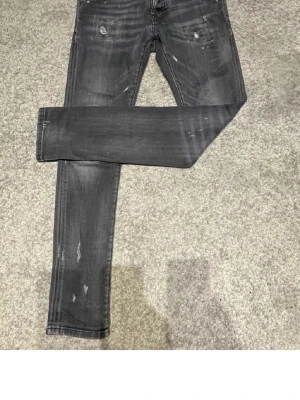 Grå slitna jeans med smal passform - Säljer ett par grå jeans med slitningar och tvättade detaljer. Jeansen har smal passform och klassisk femficksdesign. Perfekta för en avslappnad och trendig look. Materialet är troligtvis bomull med stretch för extra komfort. Storlek 12y