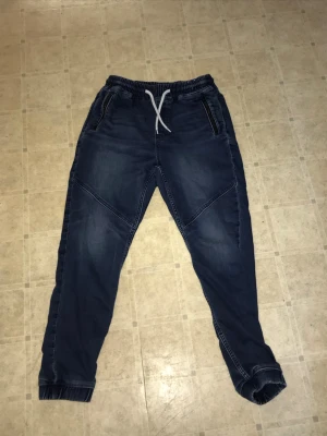 Mörkblå jogger denim mjukisbyxor - Snygga mörkblå mjukisbyxor/jeans i denim-look från Jogger Denim. Byxorna har resår, fyra fickor fram och coola sömdetaljer över benen. Perfekta för en avslappnad och trendig stil. Pris kan diskuteras.