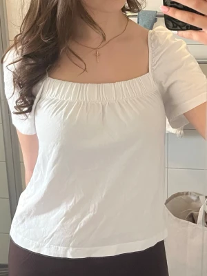 Vit puffärm topp med fyrkantig ringning - Söt vit topp med puffärmar och fyrkantig ringning både fram och bak. Den har en lätt rynkad detalj vid halsen och är i ett mjukt material💕