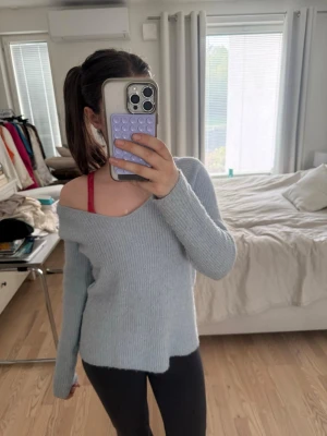 Ljusgrå off shoulder stickad tröja - Mysig ljusgrå stickad tröja med off shoulder-design och långa ärmar. Tröjan har en avslappnad passform och är ribbstickad, vilket ger en trendig och bekväm look. Perfekt att styla med jeans eller leggings.