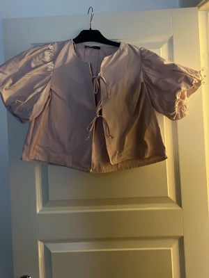 Ljuslila topp med puffärmar och knyt - Hej,jag säljer nu min jättefina rosa blus för den tyvärr inte kommer till användning.Tveka inte på att höra av er om ni har några frågor eller annat!!