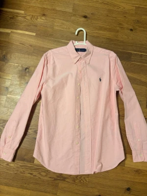 Rosa skjorta från Ralph Lauren - Klassisk rosa skjorta från Ralph Lauren med button-down krage och broderad logga på bröstet. Skjortan har långa ärmar och knäppning framtill. Tillverkad i mjuk bomull som känns skön mot huden. Perfekt för en clean och stilren look. Pris kan diskuteras!