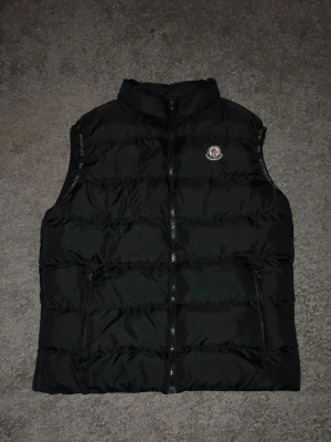 Svart dunväst från Moncler - Säljer nu en dunväst från Moncler. Västen är inte äkta, men ingen kommer frågesätta då den ser ut att vara äkta. Den värmer bra där den täcker och är i perfekt skick för nästa person. Storlek är L men borde passa för M också. Hör av er vid frågor! 