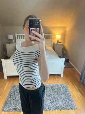 Randig vit och marinblå topp - Säljer en fräsch vit topp med marinblå horisontella ränder. Toppen har rund halsringning och korta ärmar, sitter tight och är perfekt för en stilren look. Materialet känns mjukt och stretchigt, troligtvis bomull eller bomullsblandning.