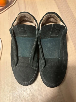 Svarta Axel arigato skor - Säljer ett par svarta Axel arigato sneakers i mocka med bred resår över vristen och diskret logga på plösen. Skorna har en låg profil och svart sula, perfekt för en clean och stilren look. Priset är inte hugget i sten hör av dig vid frågor.