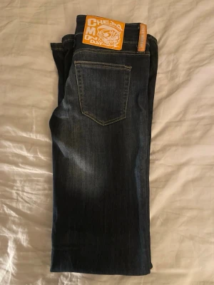 Mörkblå jeans från Cheap Monday - Säljer ett par mörkblå low waist jeans från Cheap Monday med klassisk femficksdesign och guldfärgade detaljer. Jeansen har en rak passform och är tillverkade i denim med snygga slitningar. Perfekta för en avslappnad och trendig look. Storlek W25 L32.