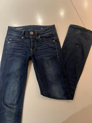Mörkblå bootcut jeans från G-Star - Snygga mörkblå bootcut jeans från G-Star med klassiska fem fickor och slitna detaljer. Jeansen har en låg midja och subtila kontrastsömmar. Perfekta för dig som gillar en avslappnad men trendig look.                                                            Fråga gärna frågor! Pris kan diskuteras!
