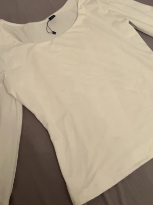 Vit långärmad topp med rund hals - En stilren vit långärmad topp med rund halsringning. Toppen har en enkel och clean design som passar till många olika outfits. Tillverkad i ett mjukt och stretchigt material för en bekväm passform.