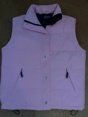 Ljusrosa väst Peak Performance - Snygg ljusrosa dunväst från Peak Performance med hög krage. Västen har tryckknappar och diskret logga på bröstet. Perfekt när det blir lite varmare men för kallt utan jacka!😍😍