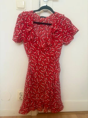 Röd blommig kortklänning med volang - Söt röd kortklänning med vitt blommönster och volangdetaljer. Perfekt för sommarens alla tillfällen! Str 38 men passar mer för någon som är 34/36