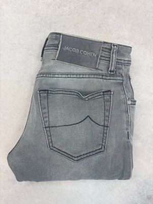Grå jeans från Jacob Cohën - Snygga grå jeans från Jacob Cohën med raka ben och klassisk femficksdesign. Jeansen har en diskret tvättad look och tydliga sömmar, samt en patch med logga bak i midjan. Perfekta för en stilren och avslappnad outfit.