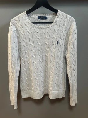 Grå kabelstickad tröja Polo Ralph Lauren - Säljer en grå kabelstickad tröja från Polo Ralph Lauren i storlek S. Tröjan har rund hals, lång ärm och klassisk broderad logga på bröstet. Mjuk och skön bomullskvalitet med ribbade muddar vid ärmslut och nederkant. Perfekt för dig som gillar stilrena och tidlösa plagg.