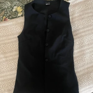 Svart väst från Gina Tricot - Stilren trendig svart väst från Gina Tricot med knappar framtill. Köpt på Arkivet och oanvänd av mig.