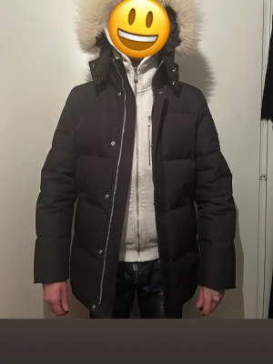 Svart dunjacka från Moose Knuckles - Säljer en svart dunjacka från Moose Knuckles med avtagbar huva och stor fluffig pälskant. Jackan har silverfärgade dragkedjor, tryckknappar och en logotyp på en ärmen. Orginal luvan utan päls medföljer 