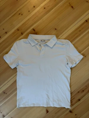 Vit Piké - Klassisk vit polotopp med krage och knappar framtill. Tidlös design som passar till det mesta och har en bekväm passform. Perfekt till jeans eller kjol för en enkel och stilren look.