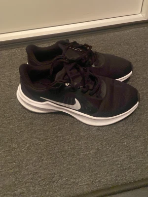 Svarta Nike sneakers med vit sula - Snygga svarta Nike sneakers med vit sula och klassisk swoosh-logga på sidan. Ovandelen är i mesh och syntetmaterial för bra andningsförmåga och komfort. Lågt skaft och snörning för en clean look som passar till det mesta.