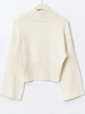 Vit croppad stickad tröja med polokrage - Snygg vit croppad stickad tröja med bred ribbad kant och hög polokrage. Tröjan har vida ärmar och är tillverkad i ett mjukt, mysigt material. Perfekt för lager-på-lager och enkel att matcha med olika outfits.