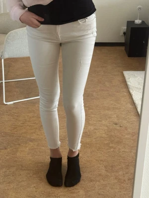 Vita skinny jeans med rå kant - Säljer ett par vita skinny jeans med hög midja och rå kant vid bensluten. Jeansen har klassisk femficksdesign och dragkedja med knapp. Snygg passform som sitter tight hela vägen ner. Perfekta till sneakers eller boots.