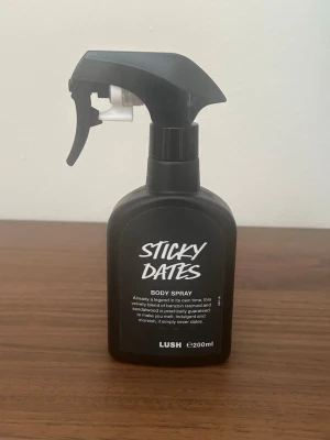 Lush Sticky Dates Body Spray 200ml - Sticky Dates Body Spray från Lush i en svart plastflaska med spraymunstycke. Doften är en söt och krämig blandning av dadel, benzoin och sandelträ. Flaskan rymmer 200 ml och har en modern, stilren design med vit text på svart bakgrund. Ca 80-90% kvar. 