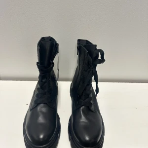 Svarta chunky kängor med snörning 42  - Stilrena svarta kängor från gabor  med chunky sula och snörning framtill. Kängorna har dragkedja på insidan för enkel på- och avtagning. Tillverkade i slätt konstläder med robust design och högt skaft. Perfekta för en edgy streetlook.