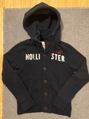 Vintage Hollister Cardigan - Väldigt sällsynt och vintage Hollister hoodie med knappar | Tröjan är i väldigt bra skick utan defekter! | Längd ≈ 63cm, Bredd armhåla-amrhåla ≈ 53cm | Modell 175cm, 68kg | Hör av vid ytterligare frågor och priset kan diskuteras vid snabbt köp! |