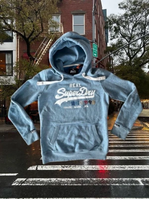 Superdry Vintage Hoodie – Archive Style - Superdry Vintage Hoodie – Archive Style Säljer en trendande Superdry hoodie i eftertraktad archive style. Plagget har en stilren ljusblå färg och en snygg vintage-look som passar perfekt för både vardag och streetwear.  🔹 Storlek: S (passar XS) 🔹 Färg: Ljusblå 🔹 Stil: Vintage / Archive 🔹 Trendande modell  📩 Skriv gärna vid frågor eller om du vill ha fler bilder.