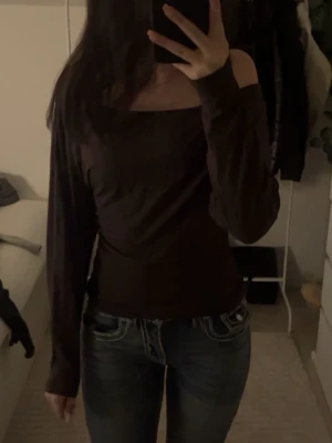 Brun offshoulder topp - Mörkbrun offshoulder topp med långa ärmar och figurnära passform. Perfekt för dig som vill ha en enkel men ändå trendig look. Tunn och mjuk i materialet, passar snyggt till både jeans och kjol.