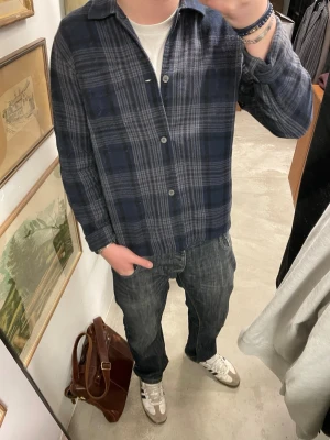 Intressekoll! Our Legacy skjorta - Säljer en blårutig skjorta från Our Legacy i mjuk bomull. Skjortan har klassisk krage, långa ärmar och knäppning framtill. Perfekt för dig som gillar en avslappnad men stilren look.