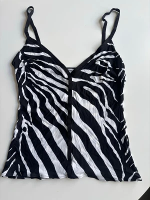 Zebramönstrat Linné från Dolce & Gabbana - Snygg body från Dolce & Gabbana med zebramönster i svart och vitt. Tunt, mjukt material och smala axelband. Djup V-ringning framtill och figurnära passform. Storleken är en blandning av S och M. 