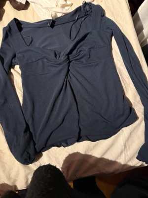 Mörkblå långärmad topp med snörning - Trendig mörkblå topp med lång ärm och snygg snörningsdetalj vid axeln. Toppen har en twistad detalj framtill som ger en cool look. Perfekt för dig som gillar en unik och stilren stil.