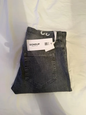 Grå skinny jeans från Dondup - Snygga grå skinny jeans från Dondup, modell George. Jeansen har klassisk femficksdesign och är tillverkade i stretchigt denimtyg för en tight passform. Perfekta för dig som gillar en modern och stilren look. W32, mått midja 40,5 | längd 102. Kvitto från nk finns, lapp sitter kvar