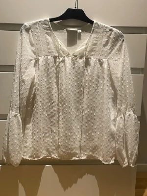 Vit blus med prickig struktur - Söt vit blus med v-ringning och långärmad design. Blusen har ett diskret prickigt mönster