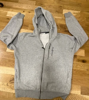 Grå sail racing Zip Hoddie - Snygg grå hoodie från sail racing   Klassisk modell med huva. Tillverkad i mjukt sweatshirtmaterial som är skönt att ha på sig.  Anledningen till att jag säljer den är att den är för liten på mig nu men annars än det inga fel på den. 