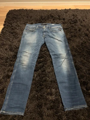 Replay anbass blå - Säljer ett par blå jeans från Replay med raka ben och snyggt slitna detaljer framtill. Klassisk femficksmodell med dragkedja och knapp. Perfekta för dig som gillar en avslappnad men stilren look.