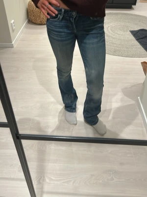 Crocker bootcut jeans  - Säljer ett par blå bootcut jeans med lätt slitna detaljer och klassisk femficksdesign. Jeansen har normal midja och är tillverkade i stretchigt denimtyg för skön passform. Perfekta för dig som gillar en avslappnad men ändå snygg stil.