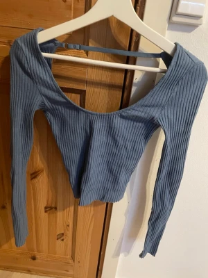 Blå ribbad croppad topp - Trendig blå croppad topp med lång ärm och ribbad struktur. Toppen har en bred, rundad urringning och är figurnära i modellen. Perfekt för att styla med höga jeans eller kjol. Den är använd några gånger men är som ny