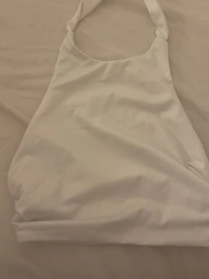 Vit halterneck linnetopp - Säljer en enkel och stilren vit halterneck linnetopp. Toppen är ärmlös och har en smickrande passform med band som knyts i nacken. Perfekt till sommaren och lätt att matcha med olika outfits.