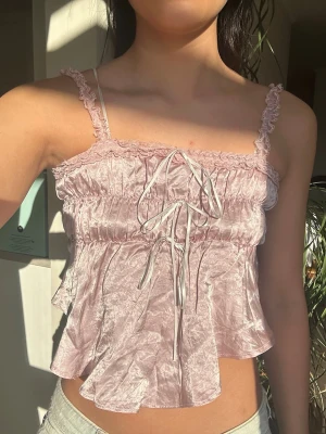 Sommar topp ljusrosa - Supergulligt linne/topp med silkes liknande material som passar i olika tillfällen. Toppen är i ljusrosa med vita och rosa lace-detaljer. Köpt i Tokyo, från butik Beams LiloCilly.   Storlek S/Xs. Resår gör toppen stretchig. Toppen är ca 33cm lång fram och baktill.  Men den är asymmetrisk (sidorna är ca 23 cm långa).   