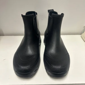 Svarta Chelsea boots i gummi från Tretorn 38 - Stilrena svarta Chelsea boots från Tretorn i vattentätt gummi. Klassisk siluett med elastiska paneler på sidorna och dragflikar bak för enkel påtagning. Perfekta för regniga dagar och ger en clean look till din outfit.