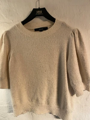 Beige stickad tröja Vero Moda - Säljer en beige stickad tröja från Vero Moda med puffärmar och rund halsringning. Tröjan har en mjuk struktur och ribbade muddar vid hals och nederkant. Perfekt för dig som gillar en enkel men trendig look.