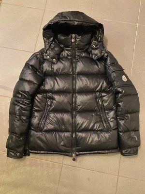 Svart Moncler pufferjacka med huva - Svart pufferjacka från Moncler maya storlek 2. Perfekt för kalla dagar.