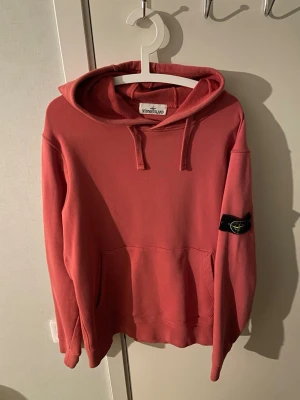 Rosa hoodie från Stone Island - Snygg rosa hoodie från Stone Island med klassisk patch på ärmen och stor känguruficka framtill. Hoodien har dragsko i huvan och en avslappnad passform, perfekt för en chill och trendig look.