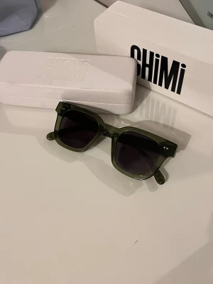 Gröna solglasögon från Chimi - Snygga solglasögon från Chimi i en trendig grön transparent färg. Modellen har rektangulära bågar och mörka linser. Kommer med originaletui och box. Perfekt accessoar för att lyfta din stil. Storlek 004